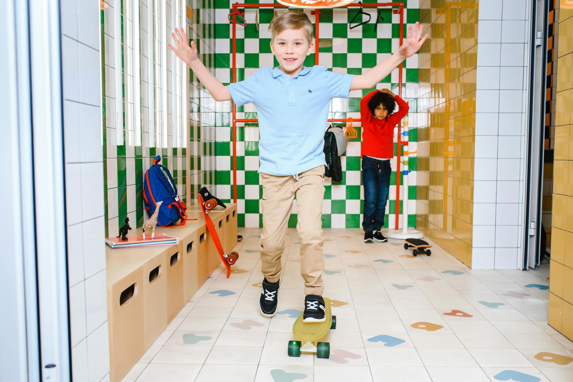 Dwoje dzieci jeździ na deskorolkach w jasnym, kafelkowanym pomieszczeniu