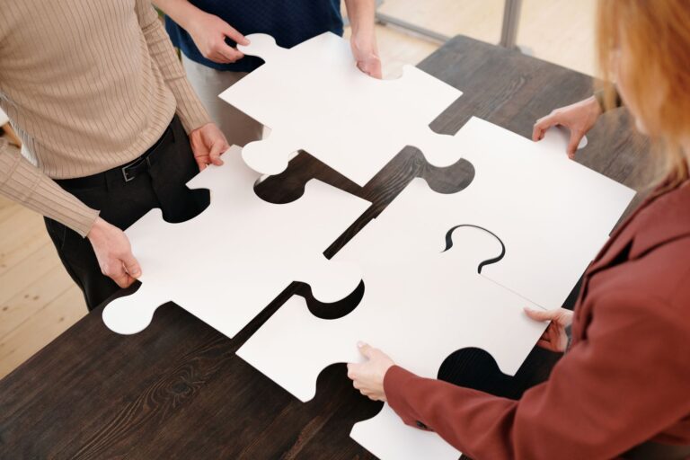 Cztery osoby układają duże białe puzzle na stole